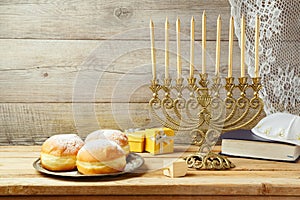 Jewish holiday Hanukkah concept with menorah, sufganiyah, gift box and spinning top on wooden table