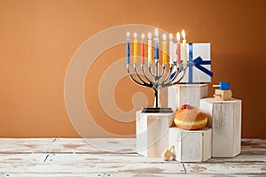 Jewish holiday Hanukkah creative concept with menorah, traditional donuts and gift box on podium on wooden table