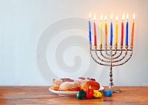 Jewish holiday Hanukkah with menorah, doughnuts over wooden table. retro filtered image