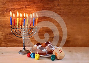 Jewish holiday Hanukkah with menorah, doughnuts over wooden table. retro filtered image