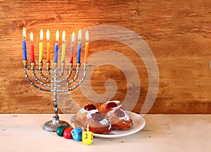 Jewish holiday Hanukkah with menorah, doughnuts over wooden table. retro filtered image.