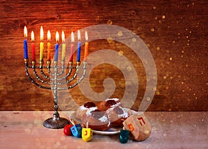 Jewish holiday Hanukkah with menorah, doughnuts over wooden table. retro filtered image