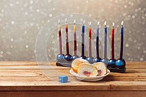 Jewish holiday hanukkah with sufganiyah and menorah on wooden table over bokeh background