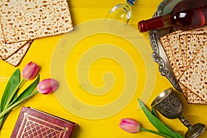 Jewish holiday Passover Pesah celebration with matzoh, tulip flowers and wine bottle on yellow wooden background.