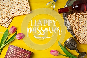 Jewish holiday Passover Pesah celebration with matzoh, tulip flowers and wine bottle on yellow wooden background.