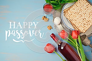 Jewish holiday Passover Pesah greeting card with seder plate, matzoh and flowers over blue background