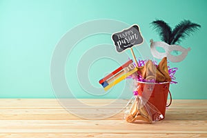 Jewish holiday Purim background with bucket, carnival mask, noisemaker and hamantaschen cookies on wooden table