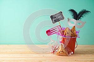 Jewish holiday Purim background with bucket, carnival mask, noisemaker and hamantaschen cookies on wooden table photo