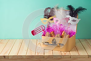 Jewish holiday Purim background with suitcase box, carnival mask, noisemaker and hamantaschen cookies on wooden table