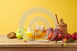 Jewish holiday Rosh Hashana concept with honey jar, apple and pomegranate on wooden table over yellow background