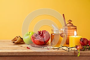 Jewish holiday Rosh Hashana concept with honey jar, apple and pomegranate on wooden table over yellow background