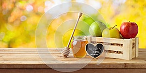 Jewish holiday Rosh Hashana concept with honey jar and apples on wooden table over nature bokeh background