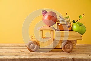 Jewish holiday Rosh Hashana concept with toy truck, honey, pomegranate and apples on wooden table over yellow background
