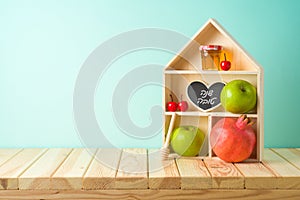 Jewish holiday Rosh Hashana creative decor background with toy house, honey jar, apple and pomegranate on wooden table