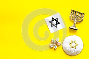 Jewish Kippah Yarmulkes hats, star of David and menorah on yellow table. Top view, copy space