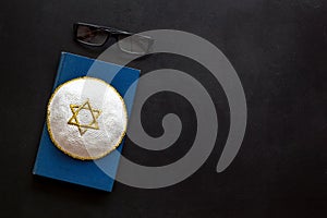 Jewish Kippah Yarmulkes hats with Star of David on Prayer book. Religion Judaisim symbols on black table. Top view