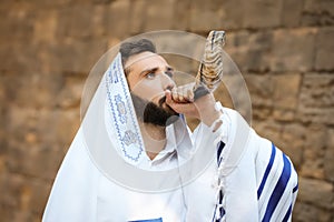 Jewish man blowing shofar on Rosh Hashanah. Wearing tallit with words Blessed Are You, Lord Our God, King Of The Universe