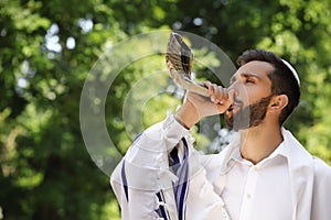 Jewish man in kippah and tallit blowing shofar. Rosh Hashanah celebration