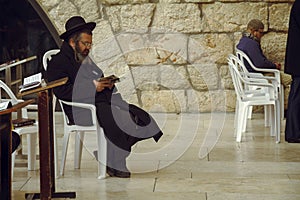 Jewish man sitting on a chair and holding bible book, praying at the sacred Wailing Wall, Western Wall, Jerusalem