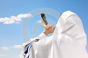 Jewish man in tallit blowing shofar outdoors. Rosh Hashanah celebration photo