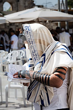 Jewish man in tallit and tefillin holding a siddur prayerbook