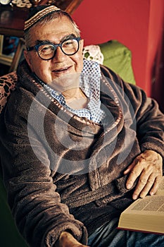 Jewish senior with glasses in the armchair reading a torah book