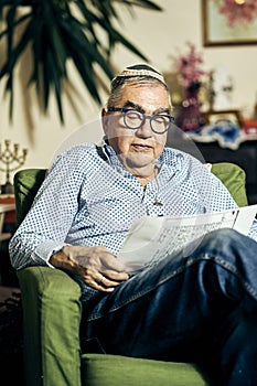 Jewish senior with glasses in the armchair reading a torah book