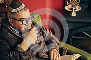 Jewish senior reading a torah book and drinking kosher wine