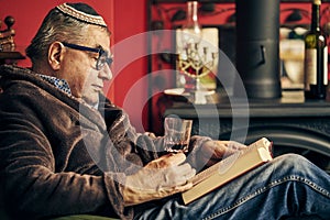 Jewish senior reading a torah book and drinking kosher wine