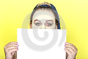 Jewish woman with blue Afro braids face in a frozen mask of green clay holding a poster on a yellow background