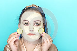 Jewish woman with blue Afro braids face in a frozen mask of green clay with pieces of cucumber in her hands