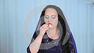 A Jewish woman with a cape on her head eats a piece of challah on Shabbat