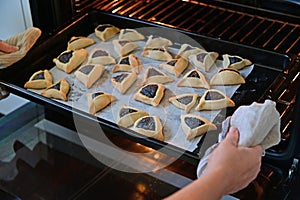 Jewish woman hands taking out baked Hamantash cookies from  kitchen oven