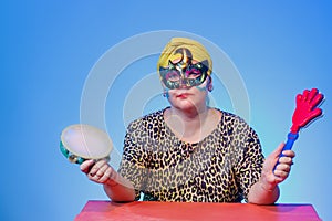 A Jewish woman in a headdress and carnival mask controls the noise on Purim while reading the scroll with a tympanum and