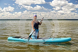 a Jewish woman in a headscarf and a pareo on a SUP board with an oar swims in the lake on a sunny day.