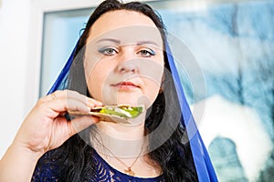 A Jewish woman with her head covered in a blue cape at the Passover Seder table is eating moror hazeret matzah. photo