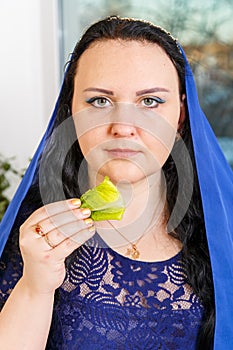 A Jewish woman with her head covered in a blue cape at the Passover Seder table is eating moror hazeret matzah. photo