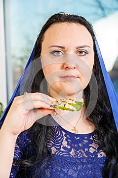 A Jewish woman with her head covered in a blue cape at the Passover Seder table is eating moror hazeret matzah. photo