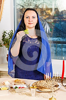 A Jewish woman with her head covered in a blue cape at the Passover Seder table is eating moror hazeret matzah. photo