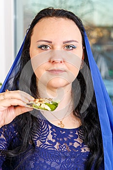 A Jewish woman with her head covered in a blue cape at the Passover Seder table is eating moror hazeret matzah. photo