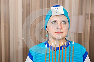 A Jewish woman in a kisui rosh headdress with a Hanukkah candlestick with burning candles in her hands mentally asks a