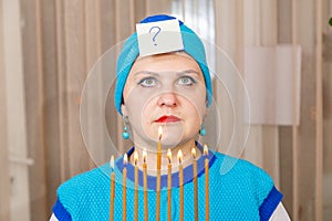 A Jewish woman in a kisui rosh headdress with a Hanukkah candlestick with burning candles in her hands is thinking