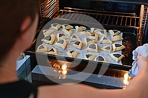 Jewish woman taking out baked Hamantash cookies from  kitchen oven