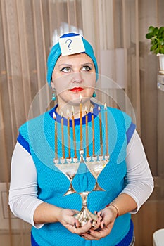 A Jewish woman wearing a kisui rosh headdress holding a Hanukkah candlestick is looking for an answer to questions about