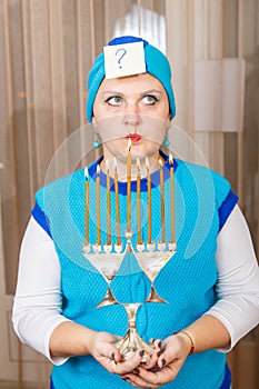 A Jewish woman wearing a kisui rosh headdress holding a Hanukkah candlestick is looking for an answer to questions about