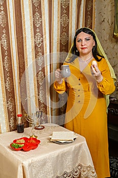 A Jewish woman in a wig and a head covering at home at the table at the Passover Seder with a beitz egg and a jug of