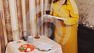 A Jewish woman in a wig and head covering makes a celebratory kiddush with a glass in her hand and a siddur.