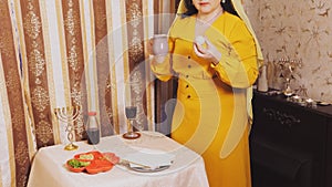 A Jewish woman in a wig and a head veil takes a beitz egg and a jug of salt water