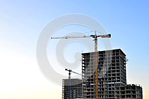 Jib construction tower crane and new residential buildings at a construction site on the sunset and blue sky background