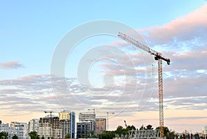 Jib construction tower crane and new residential buildings at a construction site on the sunset and blue sky background